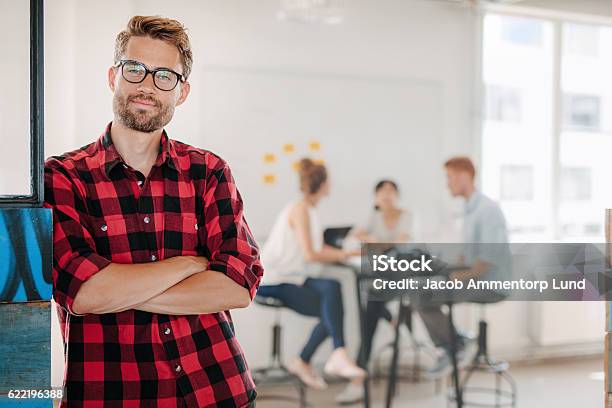 Relaxed Business Man In Office With Colleagues In Background Stock Photo - Download Image Now