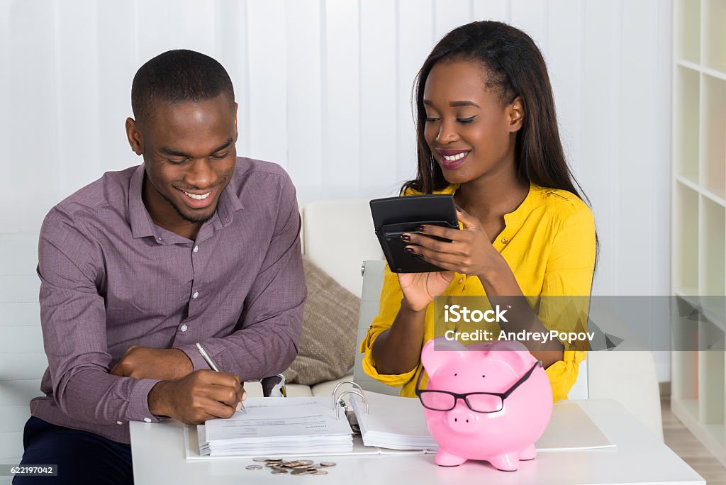 Happy Couple Calculating Bill Happy Young Couple Calculating Bill With Coins And Piggybank On Desk Savings Stock Photo