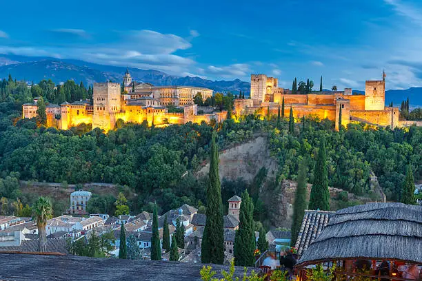 Moorish palace and fortress complex Alhambra with Comares Tower, Alcazaba, Palacios Nazaries and Palace of Charles V and roofs of Albayzin during evening blue hour in Granada, Andalusia, Spain