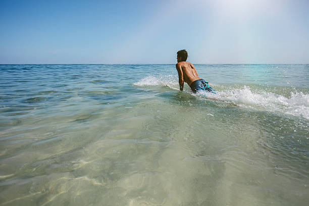 Shot of young man enjoying a surf in sea water. Male surfer in the ocean water with surf board. Man drifting on surfboard in the ocean