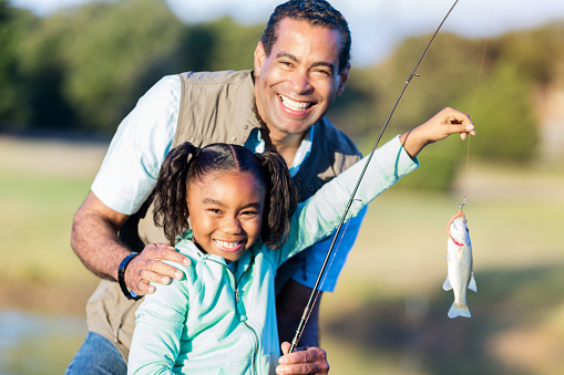Cheerful African American girl smiles proudly while holding the fish she caught with her grandpa.
