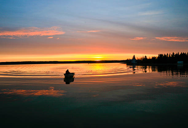 A small outboard boat silhouetted in the sunrise on Yellowknife Bay, Great Slave Lake, Yellowknife, Northwest Territories, on mirror-like water. Taken with a Canon EOS 5D and a 28-103 mm lens.