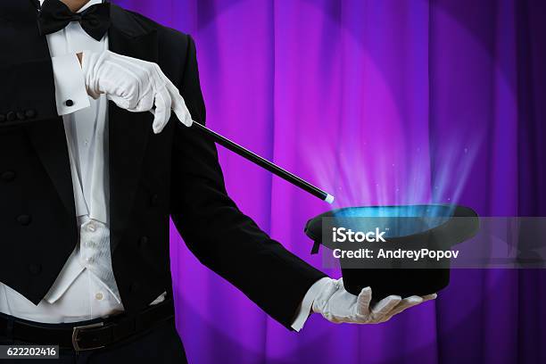 Magician Holding Wand Over Illuminated Hat Stock Photo - Download Image Now - Magician, Hat, Magic Wand