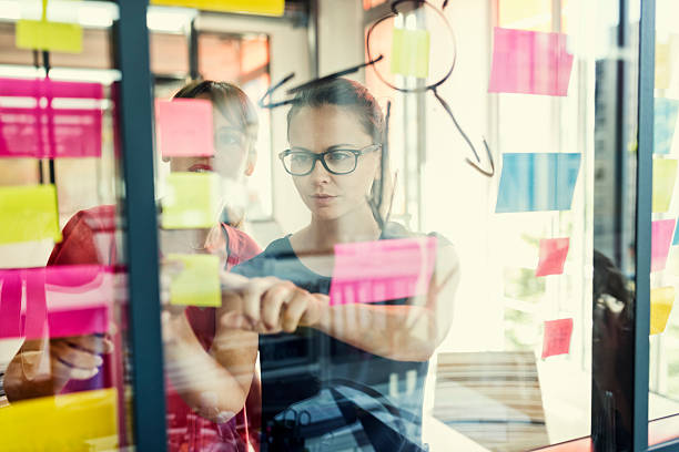 zwei geschäftsfrauen arbeiten gemeinsam an wandglas - defocused business office casual stock-fotos und bilder