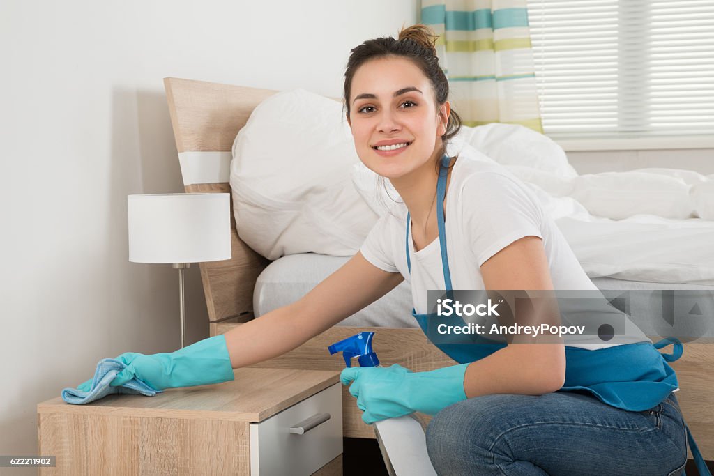 Female Housekeeper Cleaning Nightstand Happy Female Housekeeper Cleaning Nightstand In Room Cleaning Stock Photo