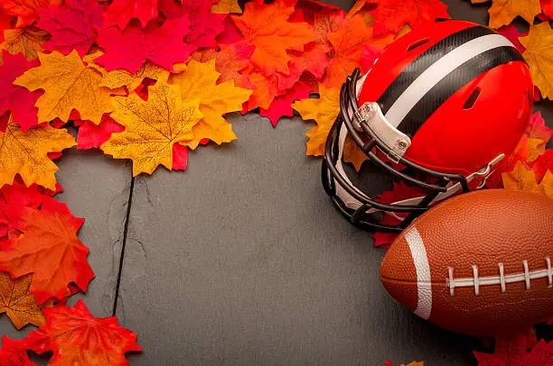 Thanksgiving american football game concept with copy space, a generic helmet and ball on the pavement surrounded by fall foliage leafs in autumn