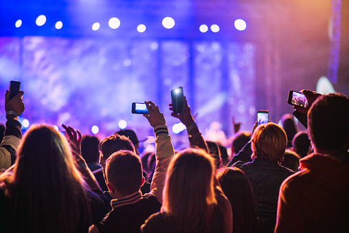 Concert goers seen from behind holding smartphones and filming a concert