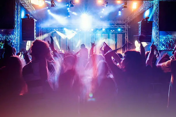 Rear view of a concert crowd with parts of the stage visible. Psychedelic colors.