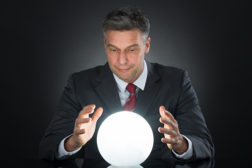 Portrait Of Businessman Predicting Future With Crystal Ball On Desk