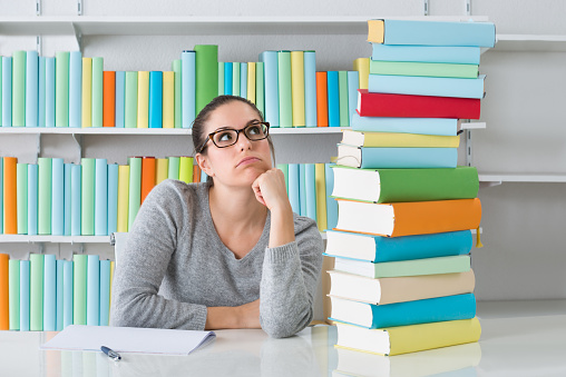 Contemplating Young Woman Sitting With Stack Of Books At Desk