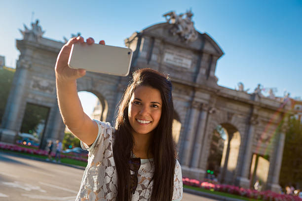 Young female tourist taking a selfie in Madrid, Spain Young latin female traveler taking a self portrayed (selfie) in the famous landmark Alcala Gate of Madrid city (Spain) in a sunny day. selfie madrid photos stock pictures, royalty-free photos & images