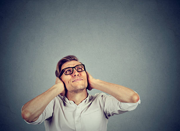stressed man covering ears looking up stop noise young annoyed, unhappy, stressed man covering his ears, looking up, stop making loud noise, giving me headache isolated on grey background with copy space. Negative emotion reaction man closing ears photos stock pictures, royalty-free photos & images