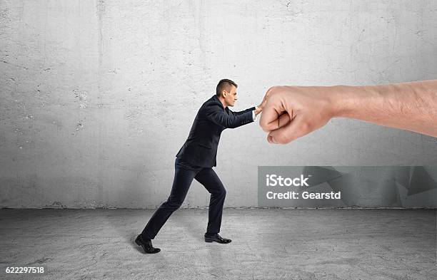 Businessman Trying To Resist Huge Male Fist And Move It Stock Photo - Download Image Now