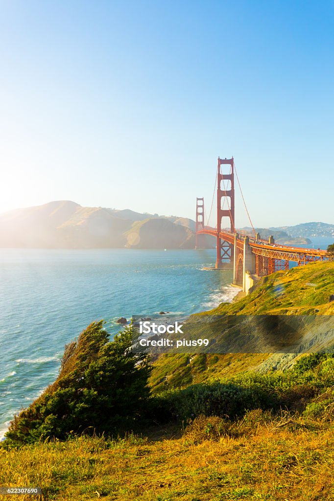 Golden Gate Bridge Marin Sunset Fort Point Coast V Sunlight provides high key highlights over Marin Headlands with Golden Gate Bridge seen over rocky coastline at Fort Point during sunset in San Francisco, California. Vertical copy space California Stock Photo