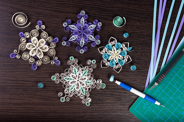 Handmade paper snowflakes with tools for quilling Handmade paper snowflakes with tools for quilling (paper strips, slotted tool, knife, cutting mat) on dark wooden background. Preparation for Christmas. paper quilling stock pictures, royalty-free photos & images