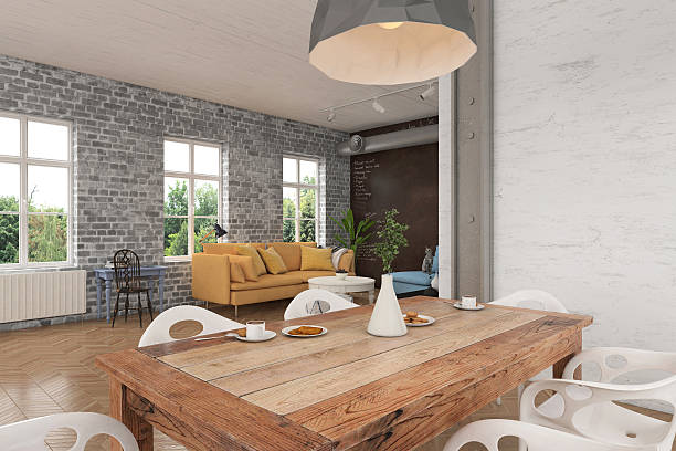 Close up view of a dining room table with white modern chairs. Modern pendant light over the table. There is a living room in the background. Windows showing nature scenery with green trees.  Brick wall dominating the scene. Horizontal composition render.