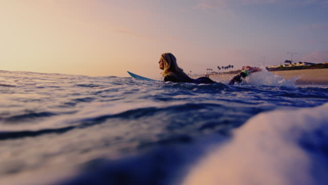 Surf girl runs out into the California ocean on surfboard shot in slow motion at sunset.