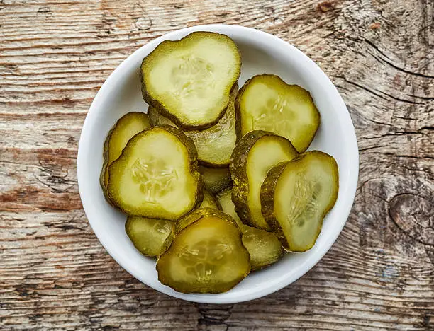 Bowl of chopped pickled cucumber on wooden background, top view