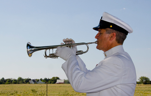 A Naval Reserve officer wears his dress whites to serve as trumpeter at a veteran's funeral, playing \