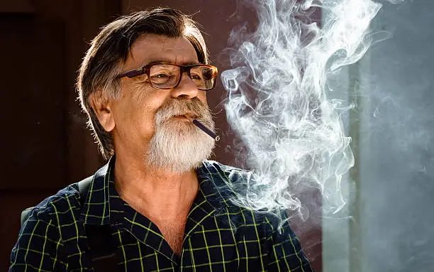 Photo of Middle-aged man with a gray beard and glasses smoke