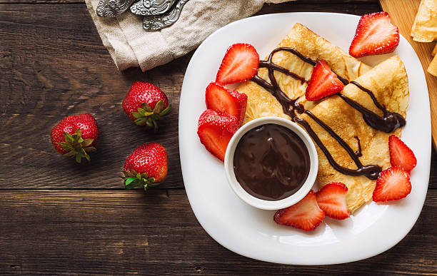 Fresh homemade crepes with strawberries and chocolate sauce Fresh homemade crepes with strawberries and chocolate sauce on rustic wooden background. Top view. blini photos stock pictures, royalty-free photos & images