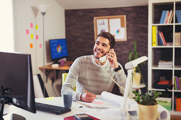 istock Young man working on computer talking on landline phone 622440064