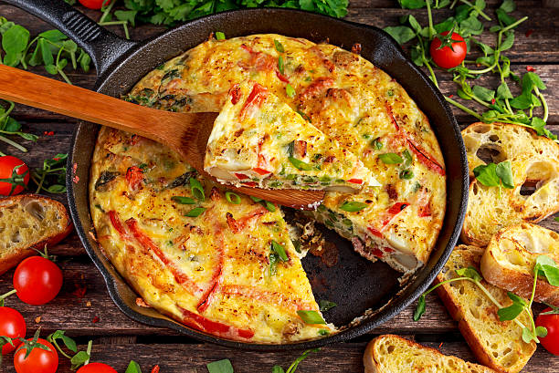Frittata made of eggs, potato, bacon, paprika, parsley, green peas Frittata made of eggs, potato, bacon, paprika, parsley, green peas, onion, cheese in iron pan on wooden table omelet rustic food food and drink stock pictures, royalty-free photos & images