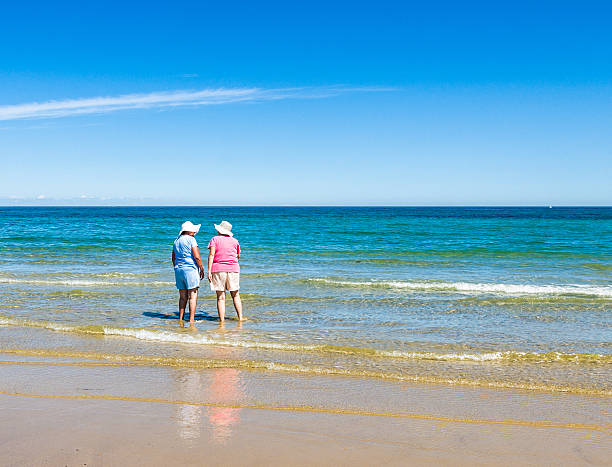 due amici sulla spiaggia - women wading sun hat summer foto e immagini stock