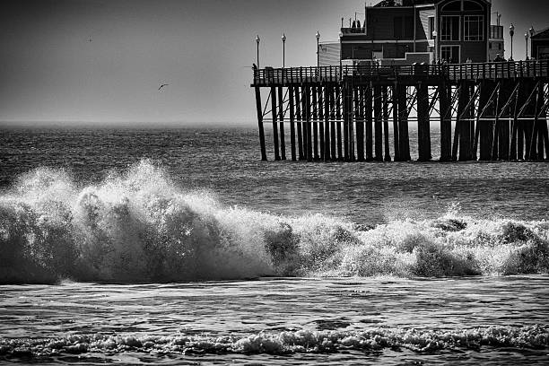 The Oceanside Pier beyond the crashing waves of the Pacific Ocean in black and white.