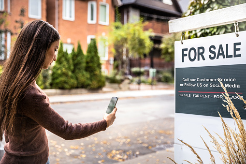 Woman photographing a real estate sign for a nice house for sale in downtown.