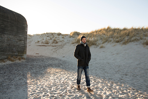Young man walking on the beach of Skagen (Denmark) near bomb shelter during sunny day backlit at the northernmost point of Denmark