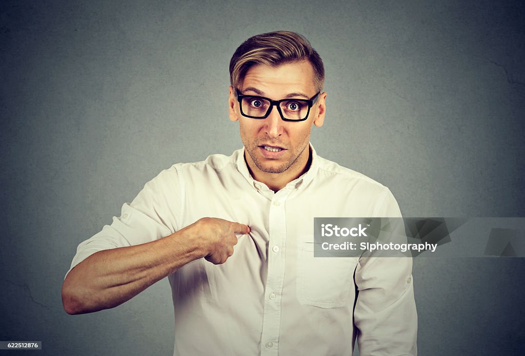 angry guy pointing at himself you mean me angry, mad, unhappy young guy pointing at himself you mean me, you talking to me, Isolated on gray background. Negative human emotion facial expression feeling Responsibility Stock Photo