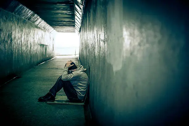 Photo of Homeless adult male sitting in subway tunnel, hands on head