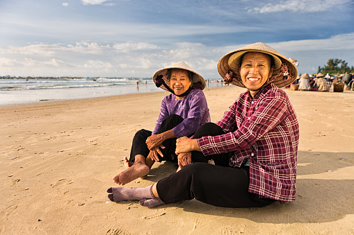 Two Vietnamese women sitting on the beach near local fish market, Vietnam.