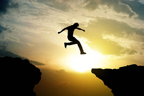 istock Man jumping over precipice on sunset background 622540214