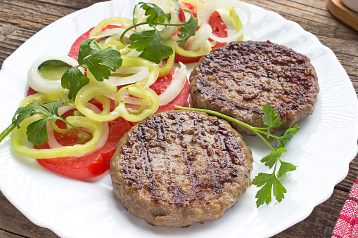 Grilled hamburger in plate with vegetable salad.