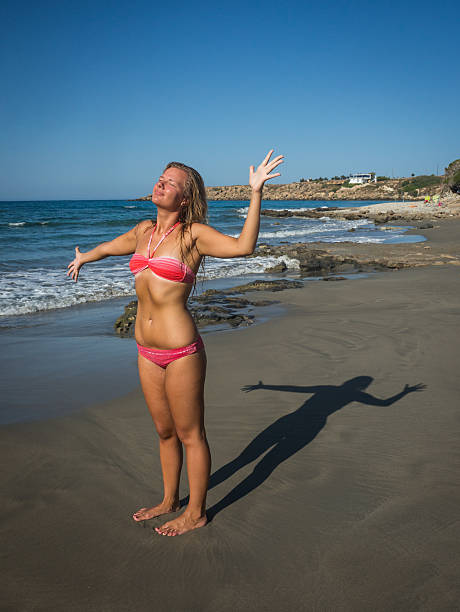Young girl in red bikini and her shadow on the beach of Crete in Greece