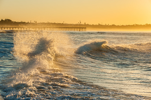 Back washed waves collide and splash with Ventura Pier in glowing background.