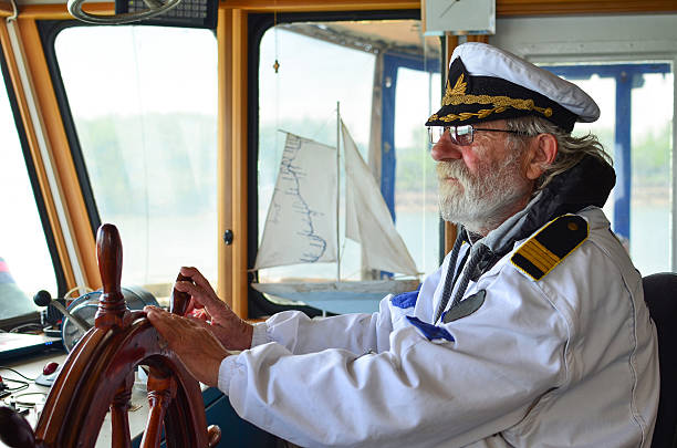 Old experienced captain in navigation cabine Ship navigation, experienced captain, old sea dog with grey hair and beard on his working place, ship navigation cabin wheel cap stock pictures, royalty-free photos & images