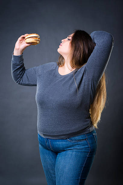 modello plus size in posa con hamburger, xxl donna che mangia hamburger - fulness foto e immagini stock