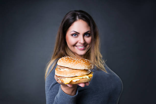 modello plus size in posa con hamburger, xxl donna che mangia hamburger - fulness foto e immagini stock