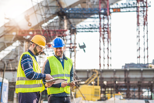 Engineers and contractors on construction site, following the progess of bridge and road infrastructure development. Two experts on construction platform in reflective wear with hardhats discussing project phases and successful previous developments. Image taken with Nikon D800 and 85mm lens, developed from RAW in XXXL size. Location: Central Europe, Europe. Copy space on right side of this image