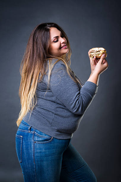 modello plus size in posa con hamburger, xxl donna che mangia hamburger - fulness foto e immagini stock