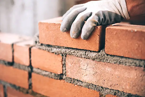 Photo of Close up of industrial bricklayer installing bricks on construction site