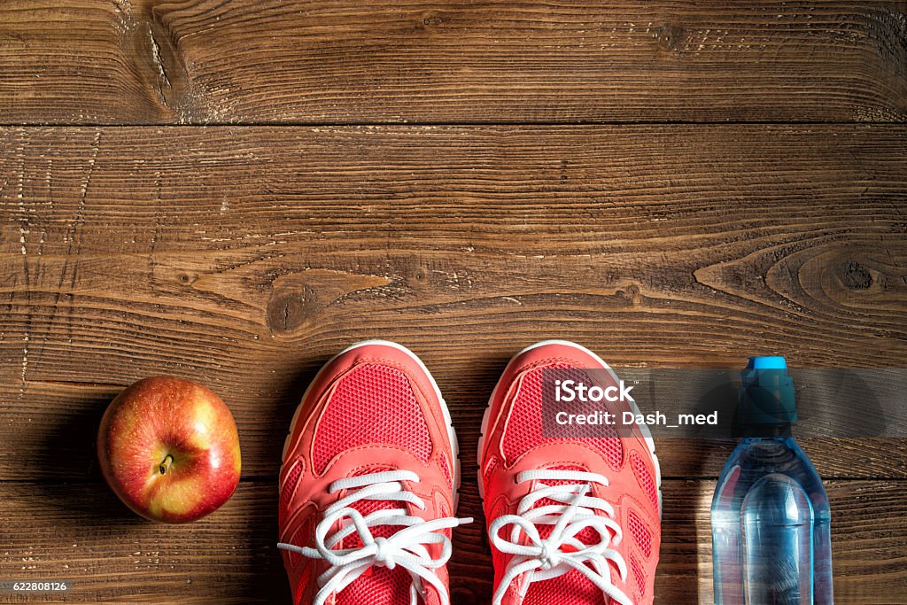 Fitness concept, pink sneakers, red apple and bottle of water Fitness concept, pink sneakers, red apple and bottle of water on wooden background, top view Apple - Fruit Stock Photo