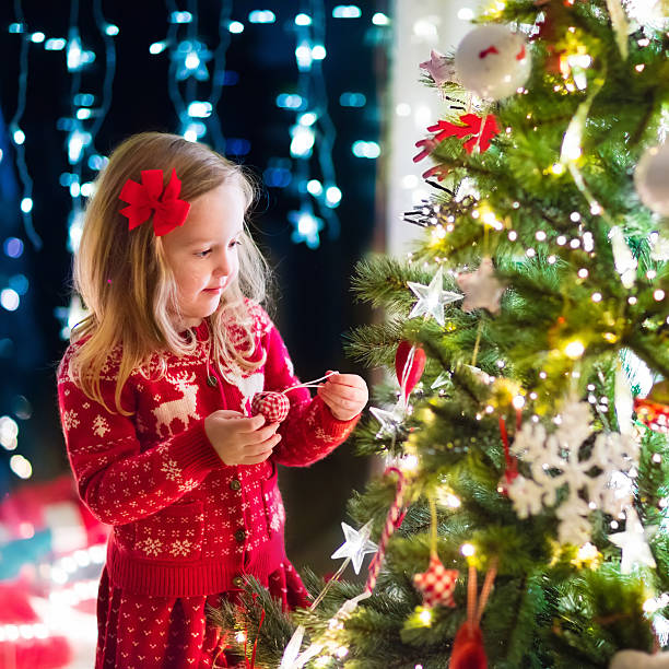 istock Child decorating Christmas tree in living room with fireplace 622810452
