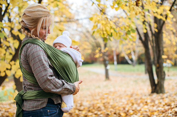 Newborn in baby sling carrier Mother and her newborn son in autumn park baby carrier stock pictures, royalty-free photos & images