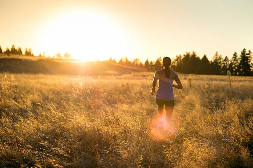 Adult African American female athlete running through tall grass as the sun sets in front of her