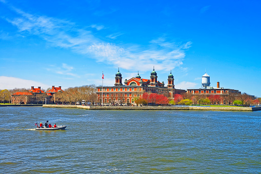 New York City, USA - April 25, 2015: Immigration station in Ellis Island, USA, and boat in Upper New York Bay. It was a gateway for immigrants who came to immigrant inspection. Tourists on board