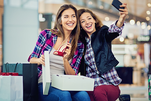 Shopping girls are looking their purchases in the Mall and taking selfie